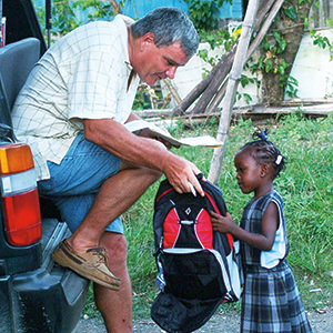 El hermano Bernard Spitzley les da a los niños pobres mochilas para la escuela.