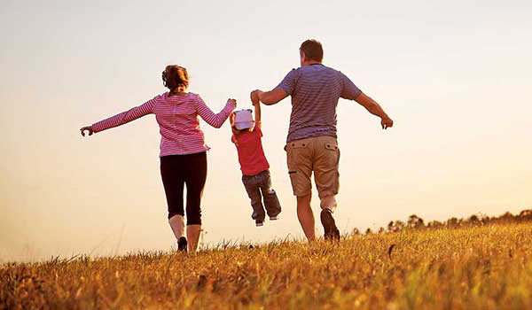 Mother and Father holding child's hands while running through field