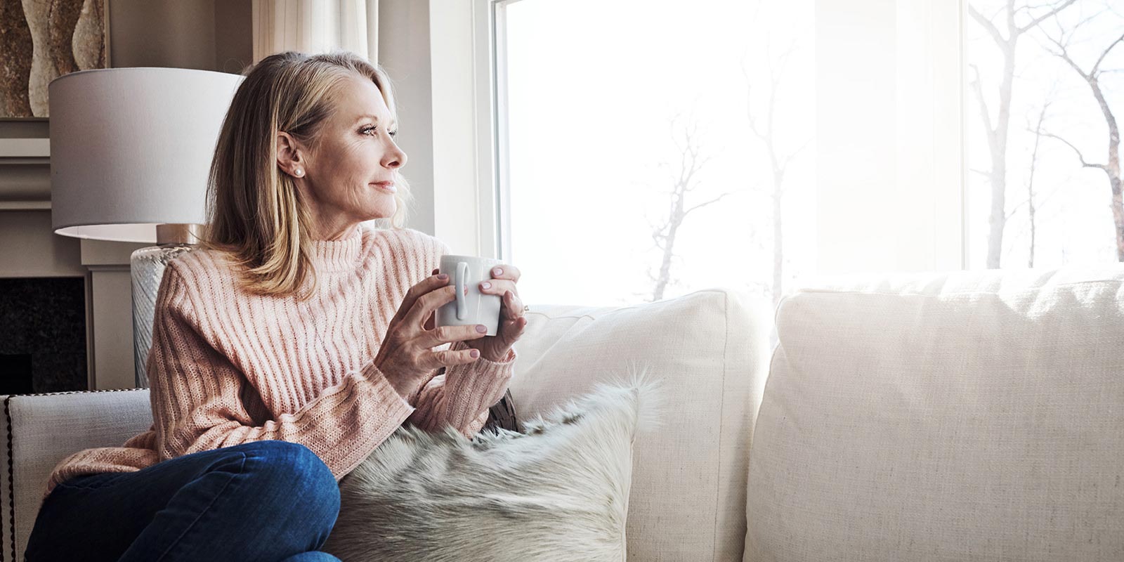 A retired woman sitting on her sofa with a coffee calmly looking at the window