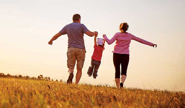 Mother and Father holding child's hands while running through field