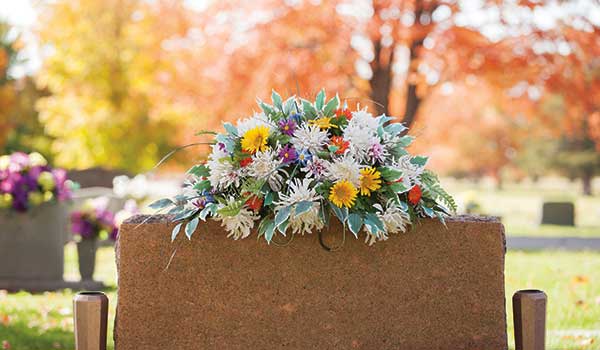 Headstone at a cemetery in the fall with flowers laying across the top