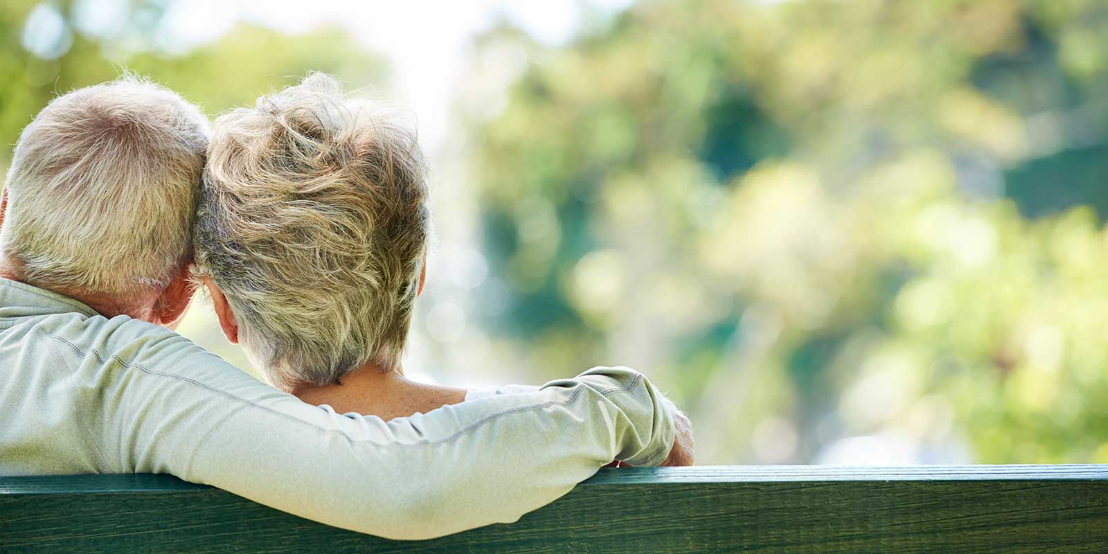 Older couple sitting on a park bench with the man's arm around the woman