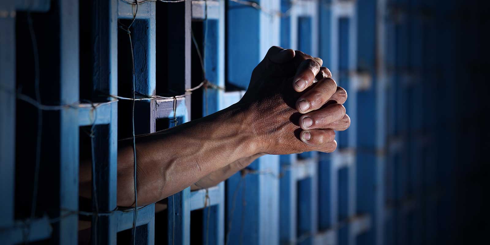 Hands grasped in prayer through prison bars.