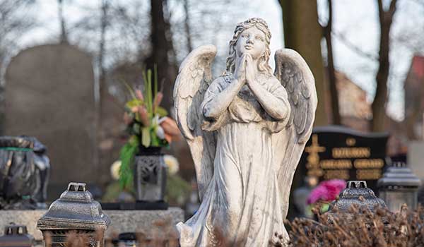 Angel statue with hands in prayer in cemetery garden.