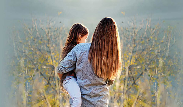 Photo of a mom carrying her young daughter through a sunlit field.