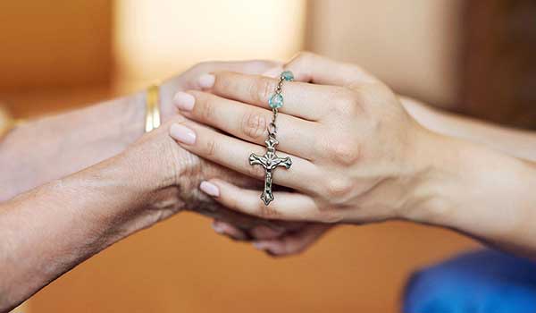 Two people holding hands with a rosary
