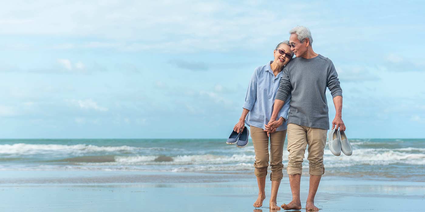 A older retired couple walking along the ocean beach smiling and holding hands