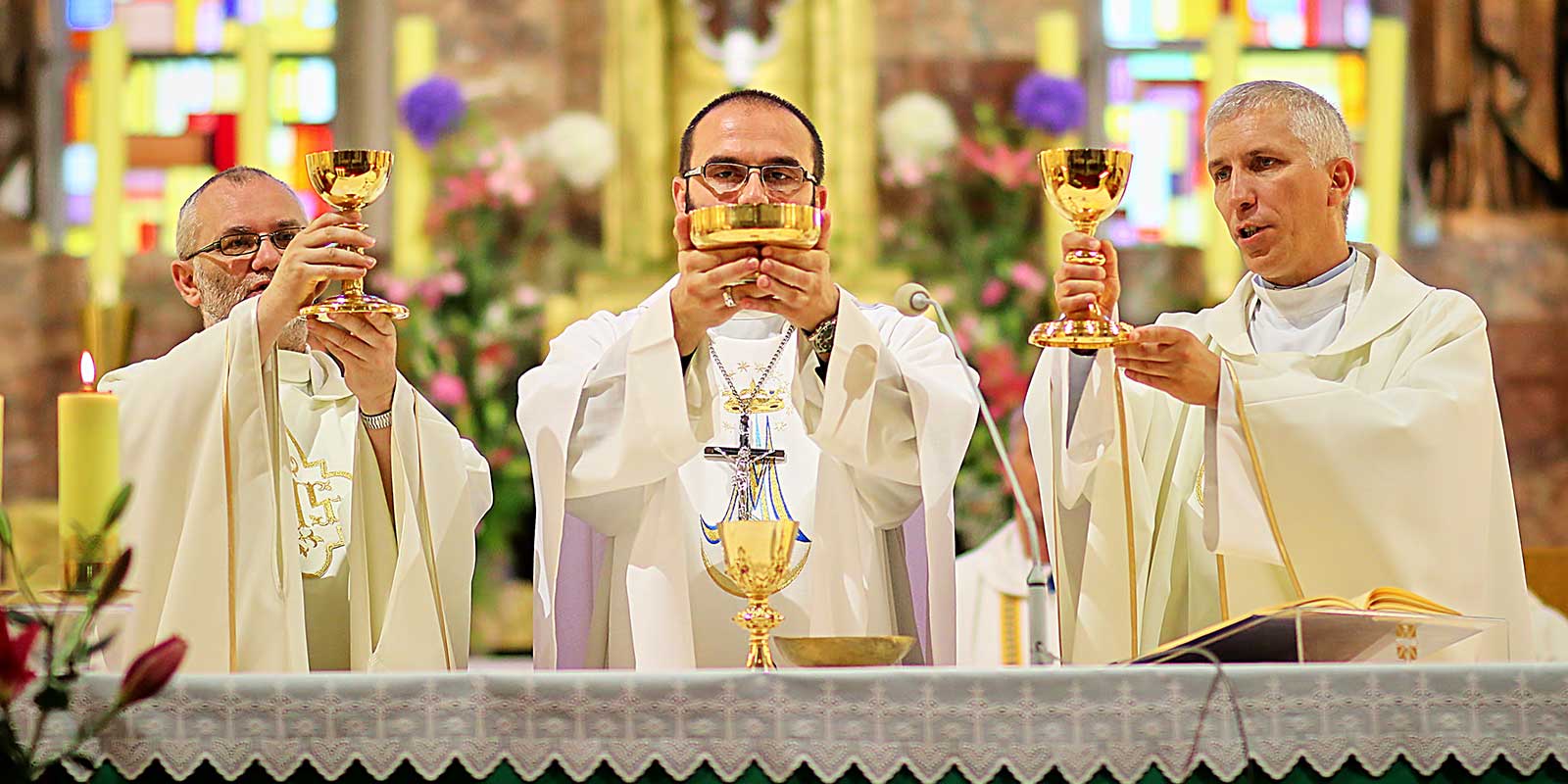 Three priests standing behind an altar holding up the Eucharist.