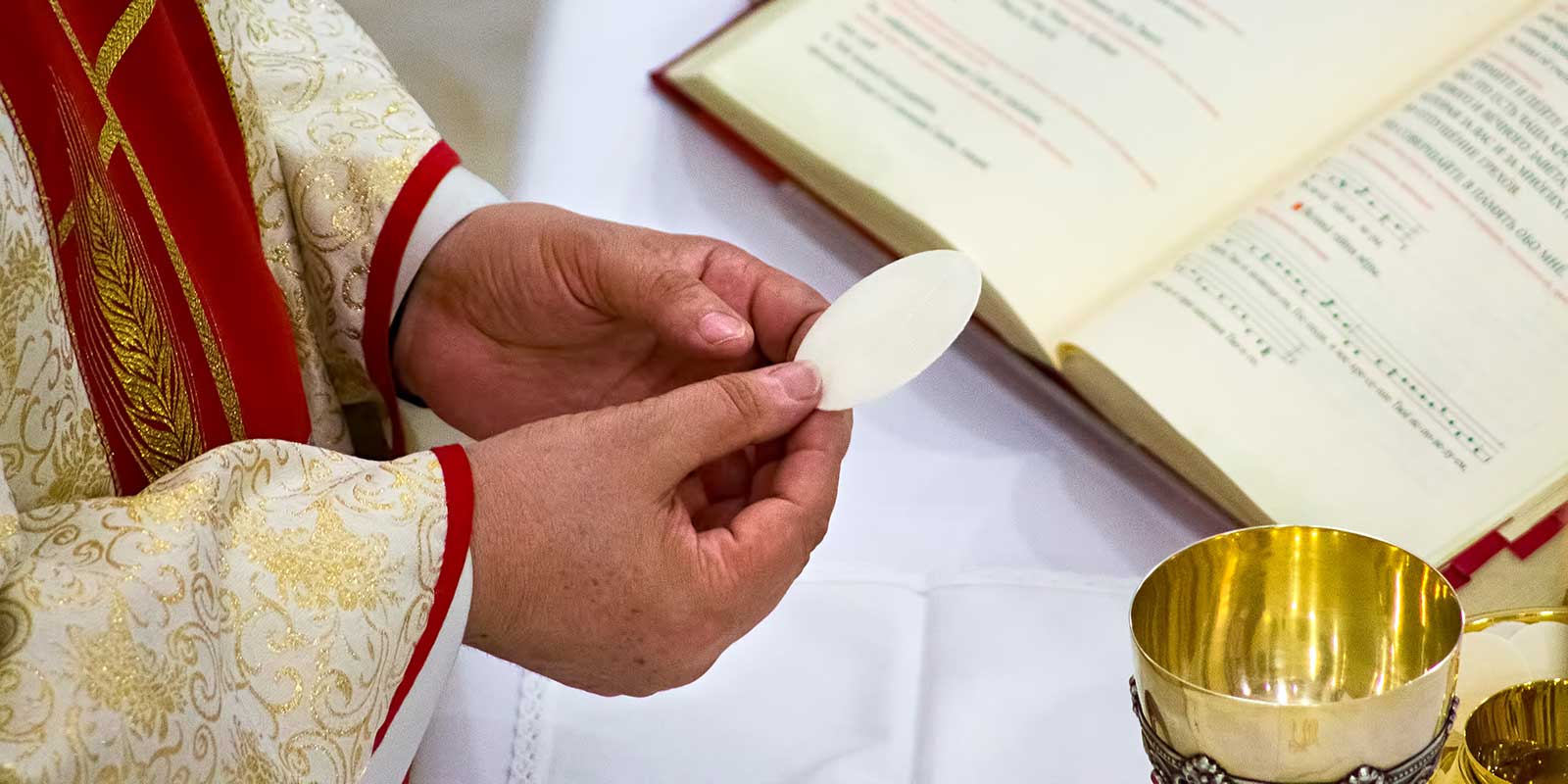 Close-up of priest's hands holding the Eucharist above the altar table.
