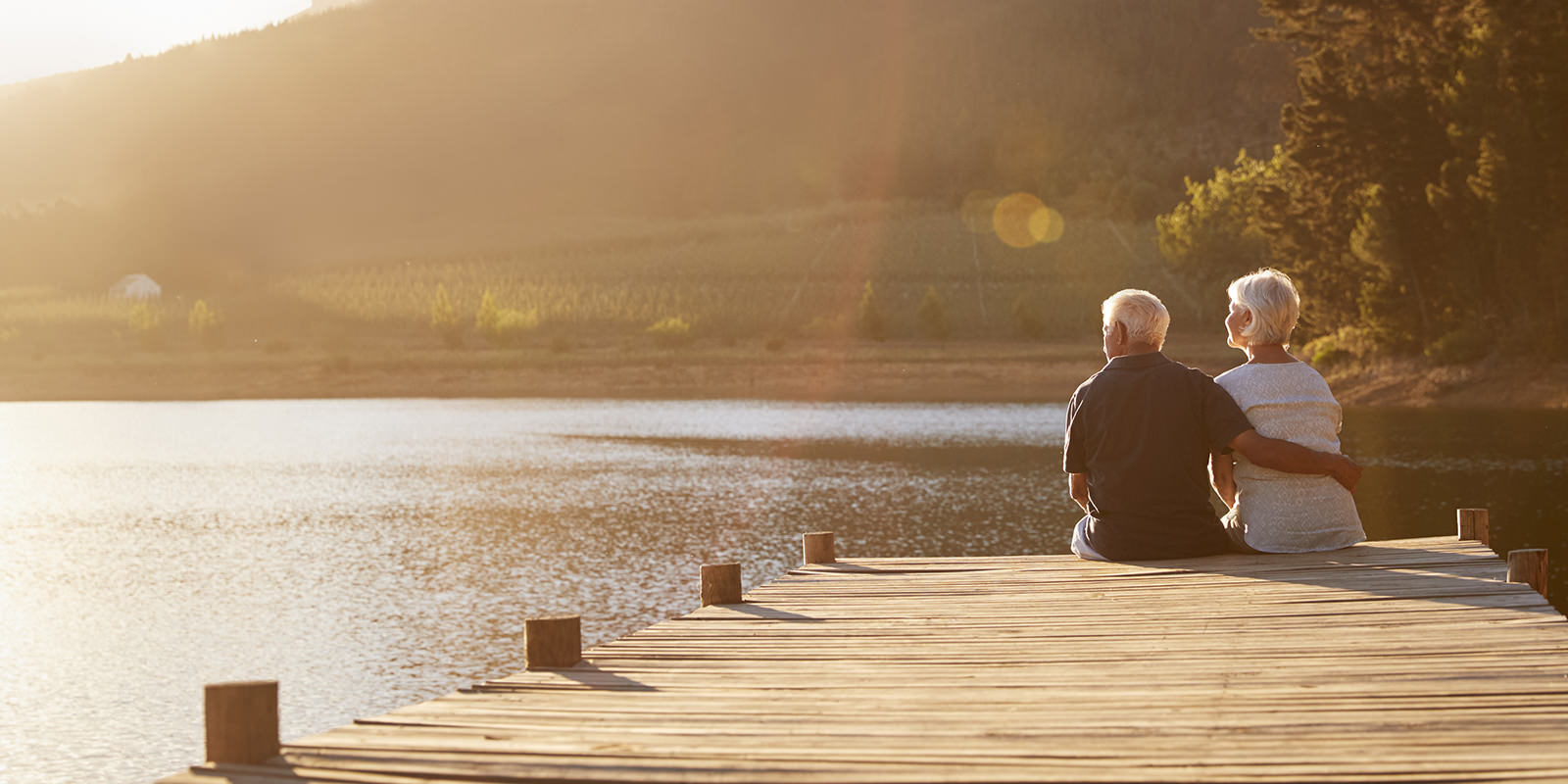 An older retired couple sits at the end of a pier on lake enjoying the scenery