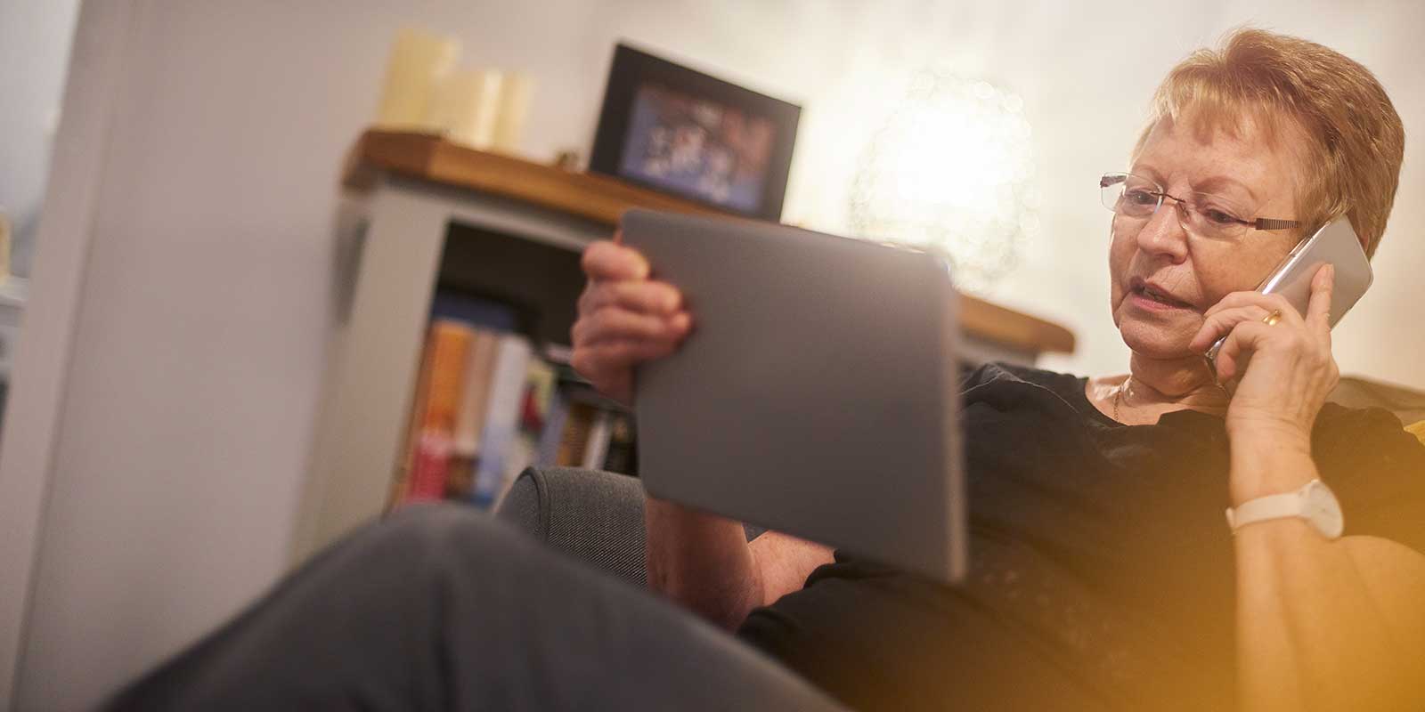 Woman sitting in living room on the phone looking at her computer table.